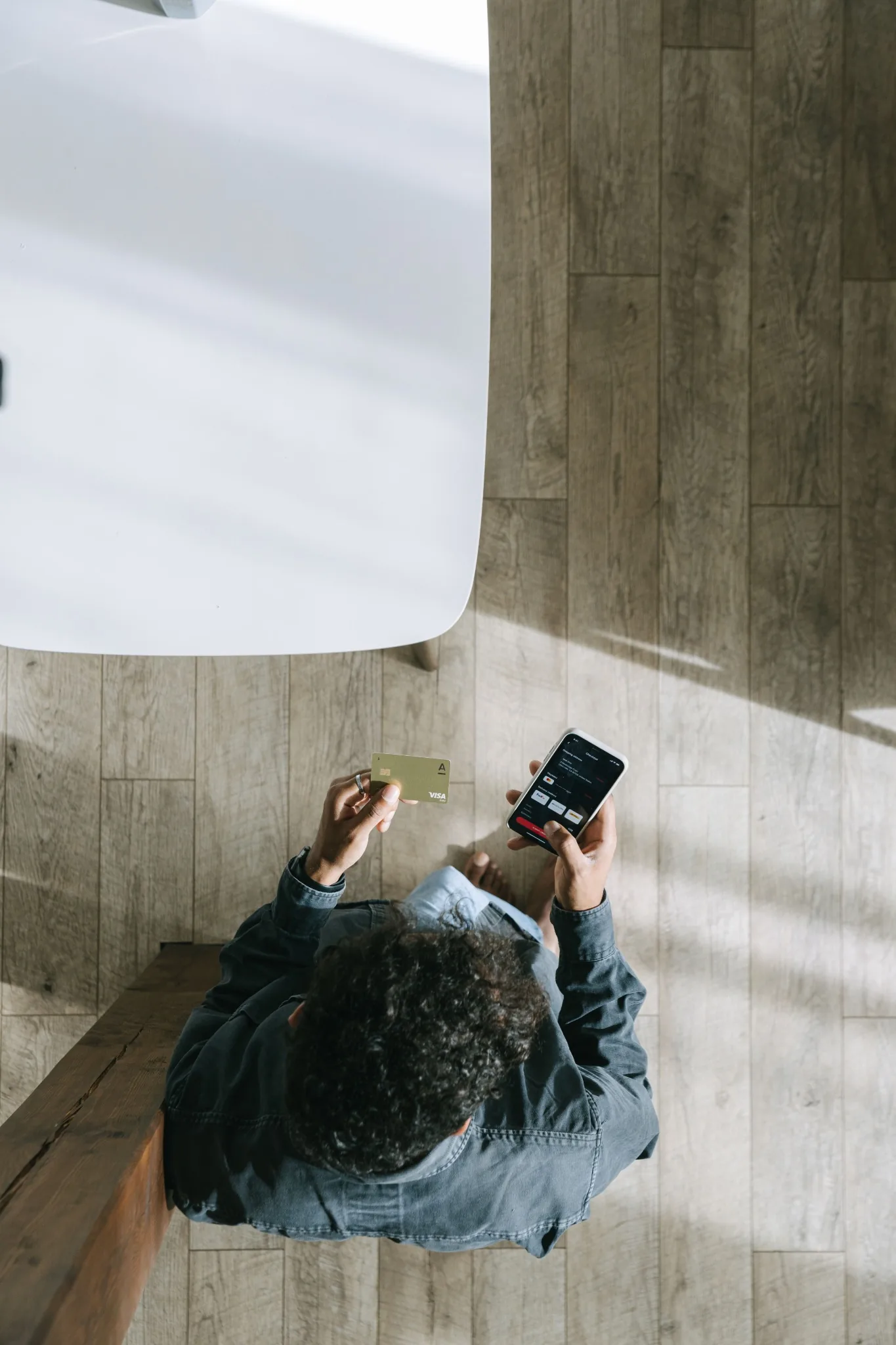 Person schaut in eine Finanz-App auf dem Smartphone und hält eine Karte in der Hand.